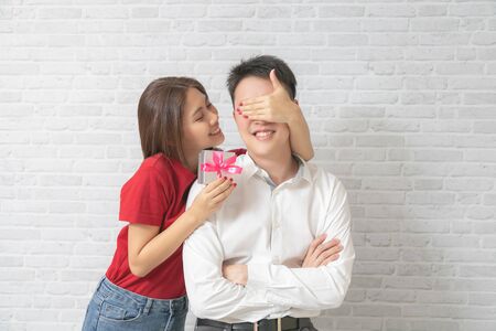 Young man receiving a surprise gift box from girlfriend at home.の写真素材