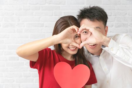 Young couple is making heart sign with hands, smiling and looking at camera. Valentine's Day concept.の写真素材