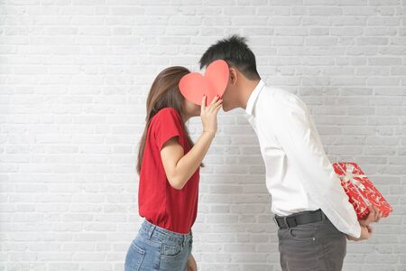 Happy young couple is kissing behind heart on blick wall background.の写真素材