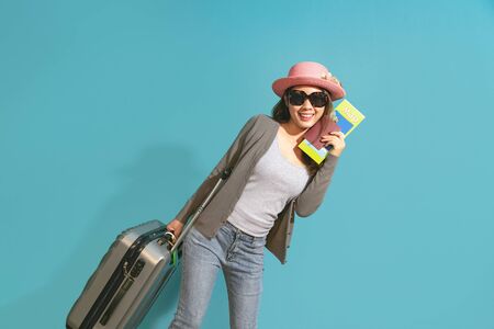 Smiling asian woman traveler holding passport with passport on blue background.の写真素材