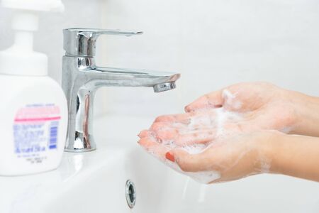 Woman hand press pure white plastic pump bottle and take cleaner foam.の写真素材