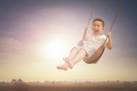 Laughing little boy riding on a swing and feeling happy in a park.の写真素材