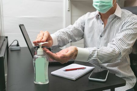 Man working from home wearing protective mask. Cleaning her hands with sanitizer gel.の写真素材