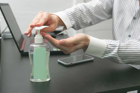 Man working from home wearing protective mask. Cleaning her hands with sanitizer gel.の写真素材