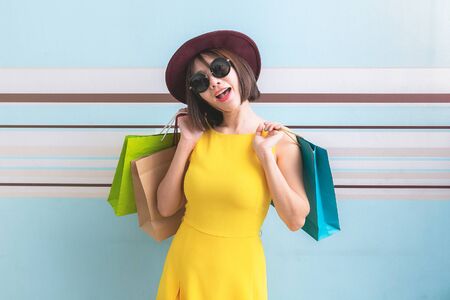 Portrait of asian beautiful girl wearing yellow dress and sunglasses holding shopping bags.の写真素材