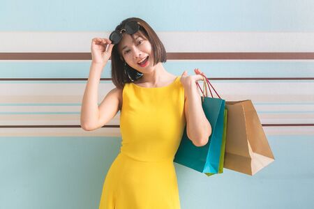 Portrait of asian beautiful girl wearing yellow dress and sunglasses holding shopping bags.の写真素材
