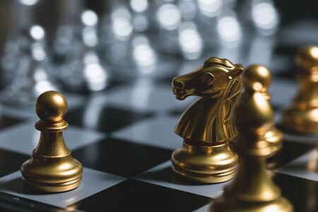 Gold pawn surrounded by gold chess pieces on a chess board.の写真素材