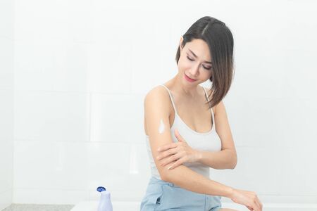 Young asian woman applying body cream at bathroom.の写真素材