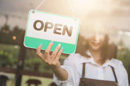 Woman hand open sign board on the door cafe or restaurant hang on door at entrance.の写真素材