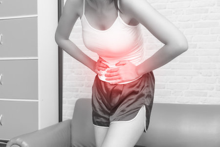 Young woman suffering from strong abdominal pain while standing on sofa at home.