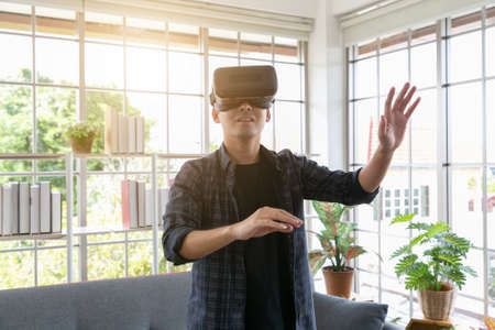Attractive young man wearing virtual reality headset or 3d glasses sitting on sofa at home.