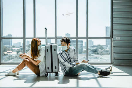 Couple asian traveler looking smartphone and sit waiting for flight at airport terminal.の写真素材