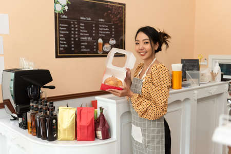 Happy asian female baker holding basket of bread, working at her bakery store. Middle aged female...