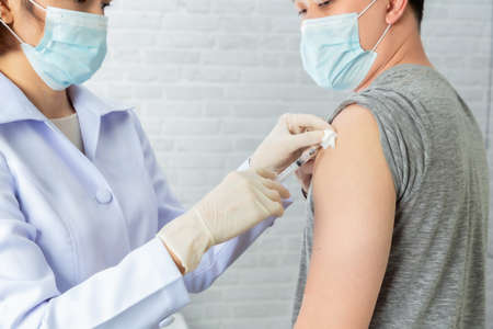 Doctor wearing protective medical mask for protection from virus disease with syringe doing injection of vaccine to patient.の写真素材