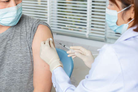 Doctor wearing protective medical mask for protection from virus disease with syringe doing injection of vaccine to patient.の写真素材