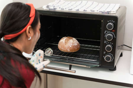 Baker woman presenting bread on board in bakery looking proudly into the camera.の写真素材