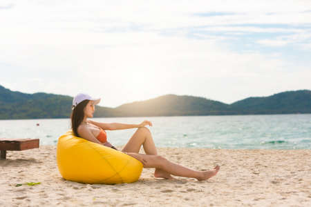 Asian woman with hat relaxing and arm up on chair beach in Thailand. Summer beach vacation concept.の写真素材