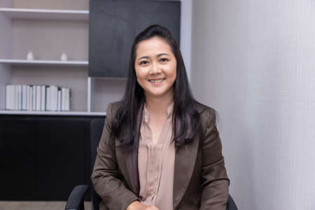 Smiling beautiful asian female professional manager sitting looking at camera, happy confident business woman corporate leader.の写真素材
