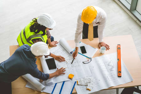 Team of Engineers architects working and standing around table working on blueprint at construction plans. Engineers discussing.の写真素材