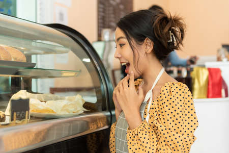 Portrait of happy asian woman choosing bread in bakery section in coffee shop.の写真素材