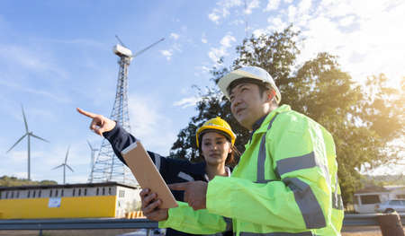 Young engineer man looking and checking wind turbines at field outdoor.
