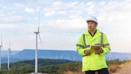 Young engineer man looking and checking wind turbines at field outdoor.