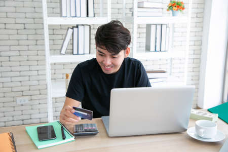 Happy Caucasian man buying things online, using  laptop and credit card, enjoying shopping in internet.の写真素材