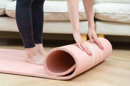Close-up of attractive young woman folding pink yoga or fitness mat after working out at home in living room.の写真素材
