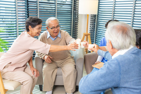 Group of happy senior friends men and women in casual sitting on couch, having conversation and drinking tea chilling together at home.の写真素材