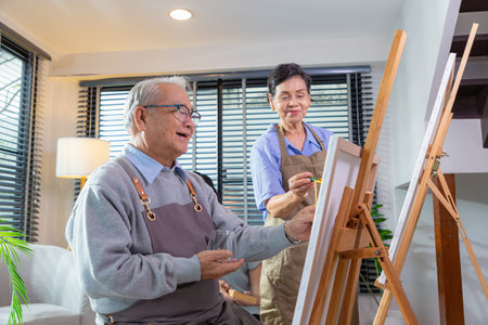 Couple Senior drawing at art. Side view portrait of white haired senior woman holding palette painting pictures at easel in art studio.の写真素材