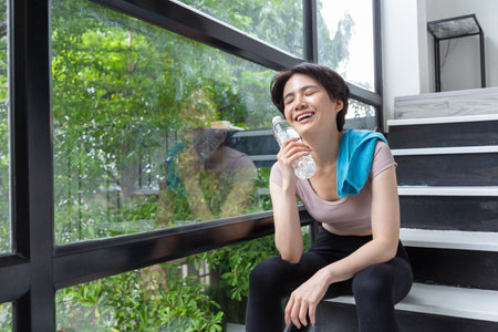Cheerful female athlete sitting on the stairl and water bottle beside her.の写真素材