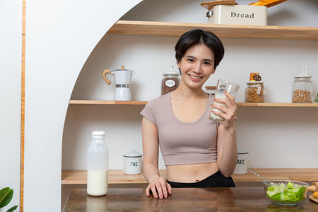 Asian young beautiful woman drinking glass of milk in kitchen at home. health care conceptの写真素材