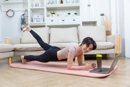 Fit asian woman doing yoga plank and watching online tutorials on laptop. training in living roomの写真素材