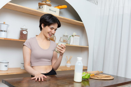 Asian young beautiful woman drinking glass of milk in kitchen at home. health care conceptの写真素材
