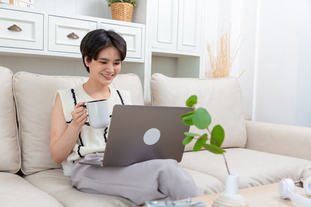 Relaxed asian woman freelancer female student browsing networks sitting on sofa looks at laptop screen.の写真素材
