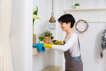 Young woman cleaning her house, she is dusting a shelf, chores and hygiene conceptの写真素材
