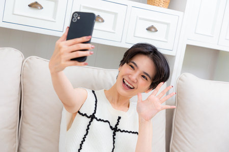 Image of beautiful asian woman laughing and showing peace sign while taking selfie photo on cellphone.の写真素材