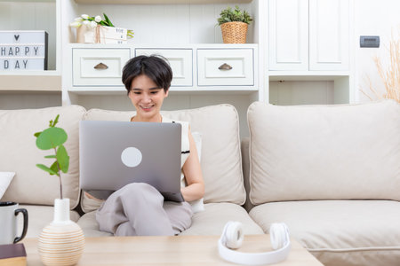 Relaxed asian woman freelancer female student browsing networks sitting on sofa looks at laptop screen.の写真素材