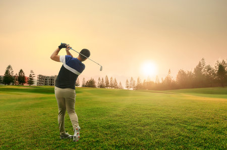 Man playing golf on a golf course in the sunrise. View from the back.の写真素材