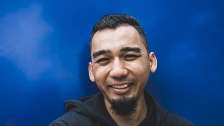 Closeup shot of happy young man smiling in blue backgroundの写真素材