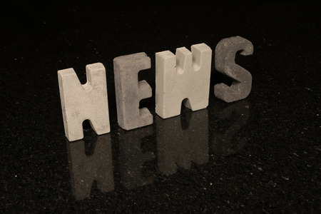 The word News spelled with grey concrete letters on black reflecting tile