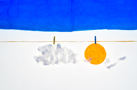 composition with blue sky clouds and sun made with tissue paper, a rope, small pegs for hanging the laundryの写真素材