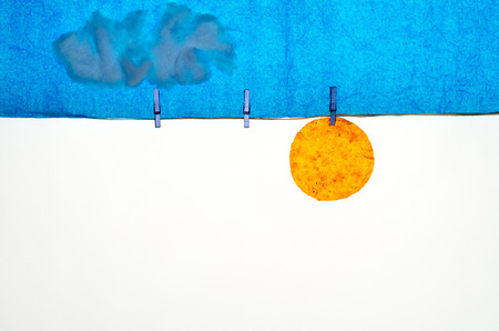 composition with blue sky clouds and sun made with tissue paper, a rope, small pegs for hanging the laundryの写真素材
