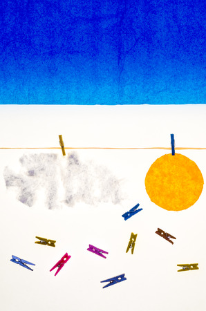 composition with blue sky clouds and sun made with tissue paper, a rope, small pegs for hanging the laundryの写真素材