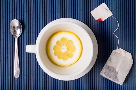 simple composition with tea cup empty but with slice of lemon, saucer and spoon, filter bag of tesu blue striped backgroundの写真素材
