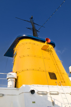 Yellow ship funnel with a red speaker on side. There are ladders around the funnel and some ventilation grids in it.の写真素材