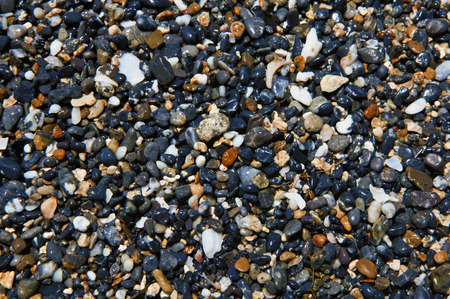 Wet stones on the seashore. They are black, grey, pink, yellow, and off-white.