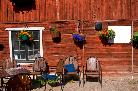 A small countryside cafe outside Uppsala, Sweden. There are some wooden tables and chairs outside a Falu red house. There are some plants on the house wall.の写真素材