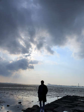 A boy standing against a background of cool clouds and sea