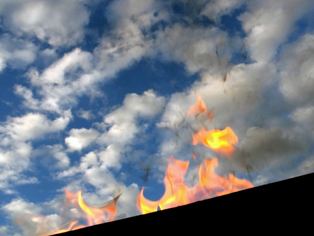 Firewood and fire in the old rusty charcoal grill on blue sky and clouds backgroundの写真素材